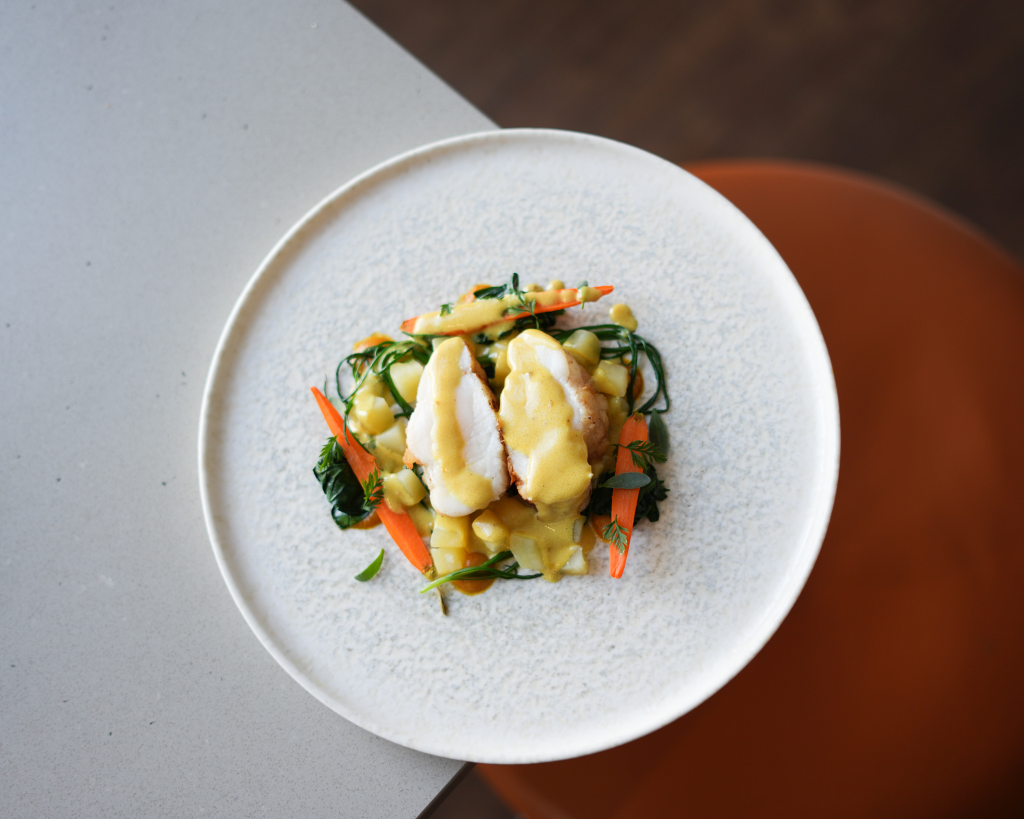 Plated spiced katsu monkfish with seasonal vegetables and a lentil dressing.