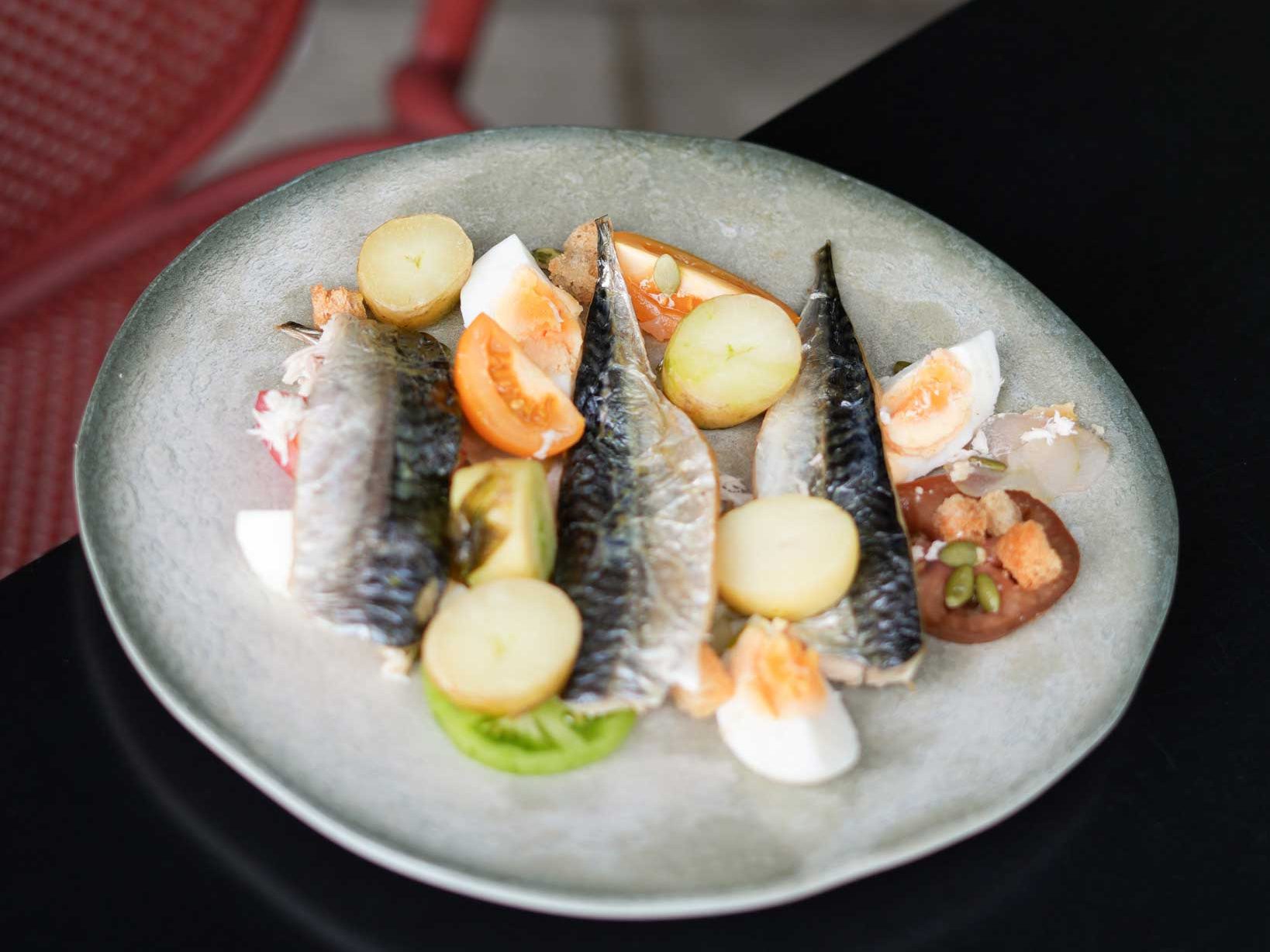Plate of grilled mackerel with boiled potatoes, tomatoes, eggs, and croutons.